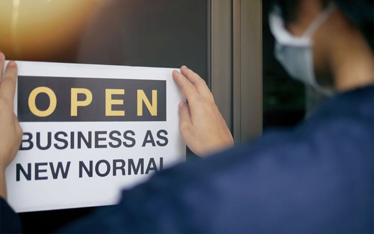 worker posting sign that says 'open business as new normal'