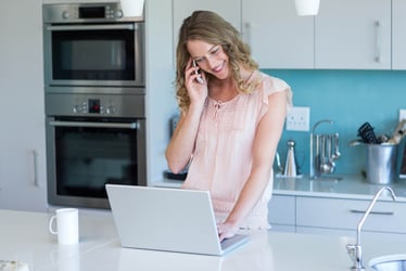 woman using a laptop and on the phone at home in her kitchen