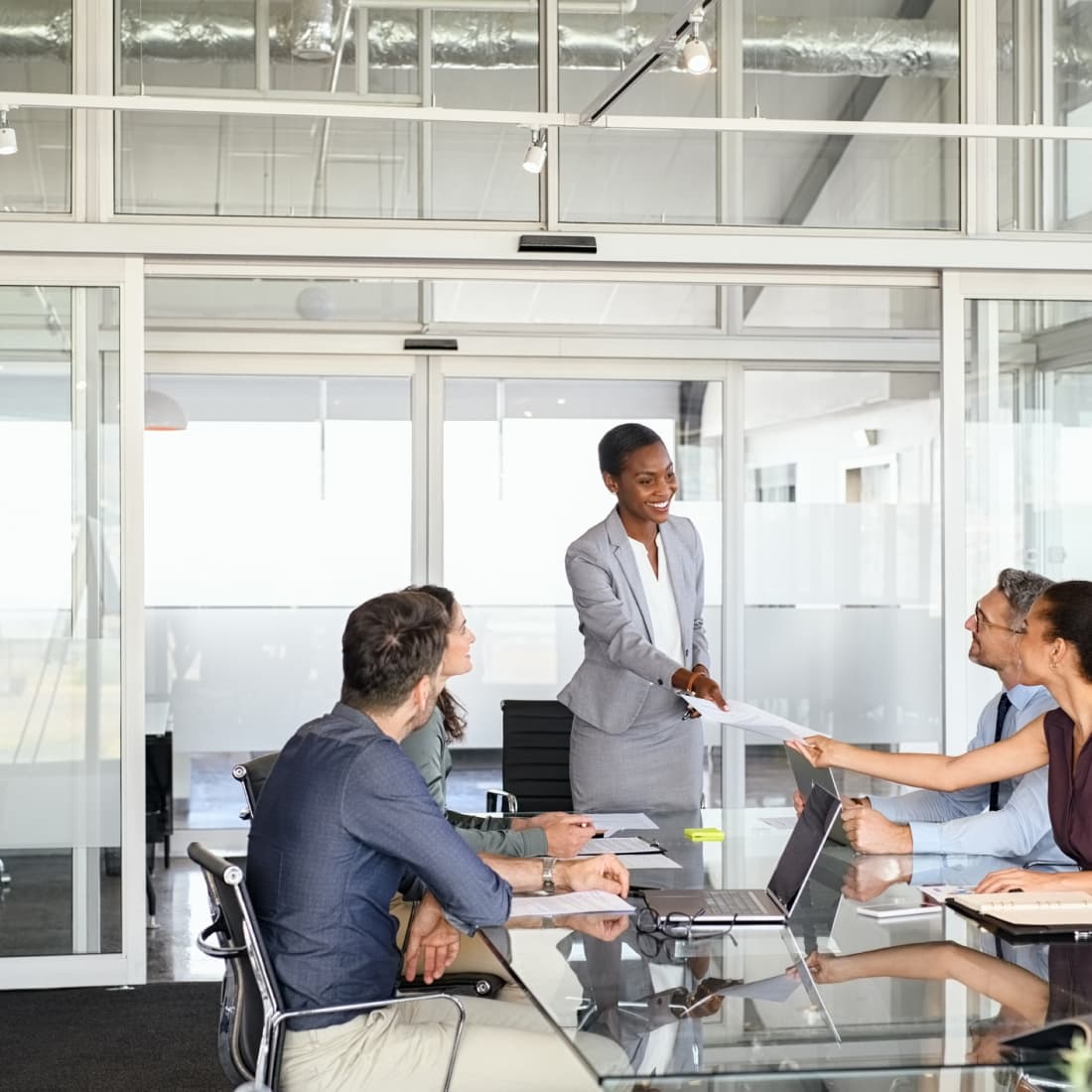 Business woman standing to hand paperwork to coworker during meeting. 