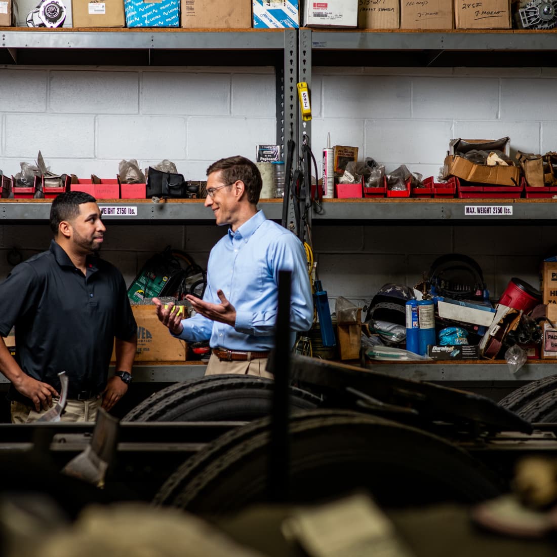 Two men conversing in mechanical warehouse. 